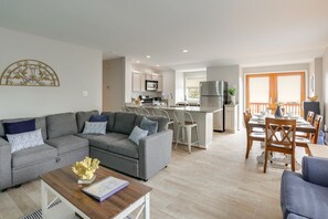 A modern living room with a grey sofa, a wooden coffee table, and a dining area with wooden chairs and a table.
