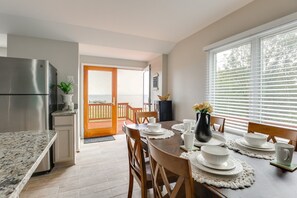 A kitchen with a stainless steel refrigerator, wooden dining table set with white plates and bowls, and a view of the ocean through a glass door. - Kent Island Waterfront Cottage (Stevensville)