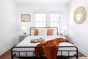 A neatly arranged bedroom with a bed, two bedside tables, a wall-mounted mirror, and a framed picture. - Bohemian Bliss (Atlanta)