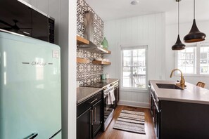 A modern kitchen with a light blue refrigerator, stainless steel appliances, and a large window providing natural light.