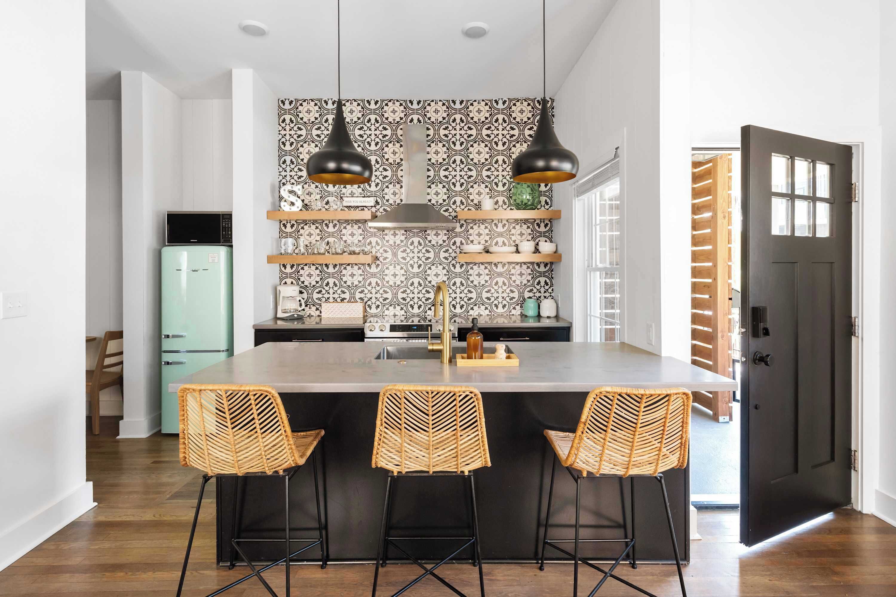A modern kitchen with a central island, pendant lights, and a patterned backsplash.