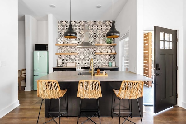 Una cocina moderna con una isla central, luces colgantes y un salpicadero con estampado.