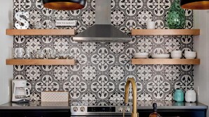 A modern kitchen with patterned backsplash, stainless steel appliances, and wooden shelves. - Bohemian Bliss (Atlanta)