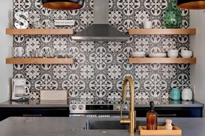 A modern kitchen with patterned backsplash, stainless steel appliances, and wooden shelves.