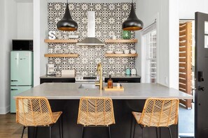 Une cuisine dotée d’un îlot central, de chaises noires et d’un crédence à motifs.