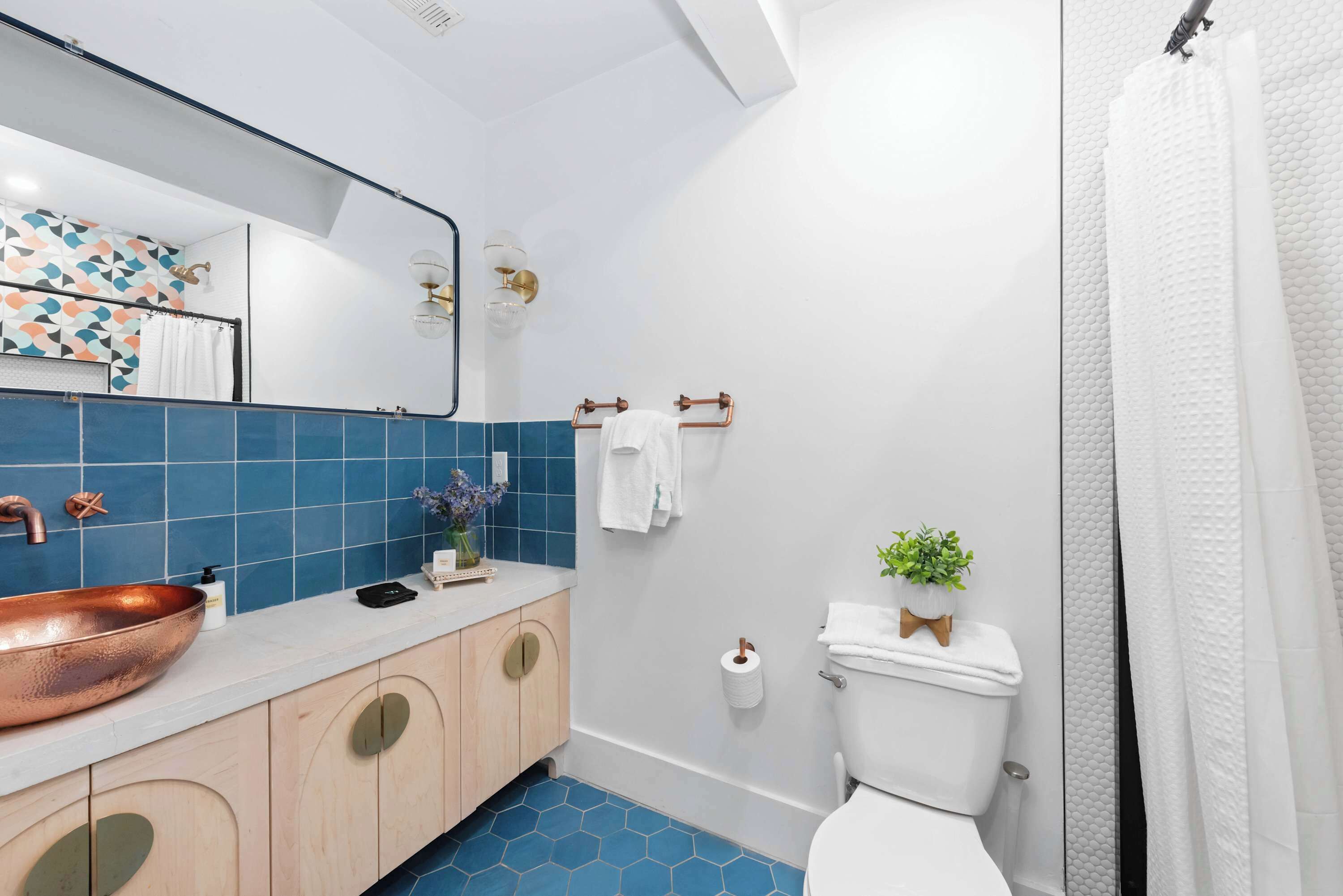 A bathroom with a copper sink, blue hexagonal tiles, a white toilet, and a shower curtain.