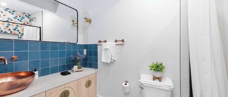 A bathroom with a copper sink, blue hexagonal tiles, a white toilet, and a shower curtain.