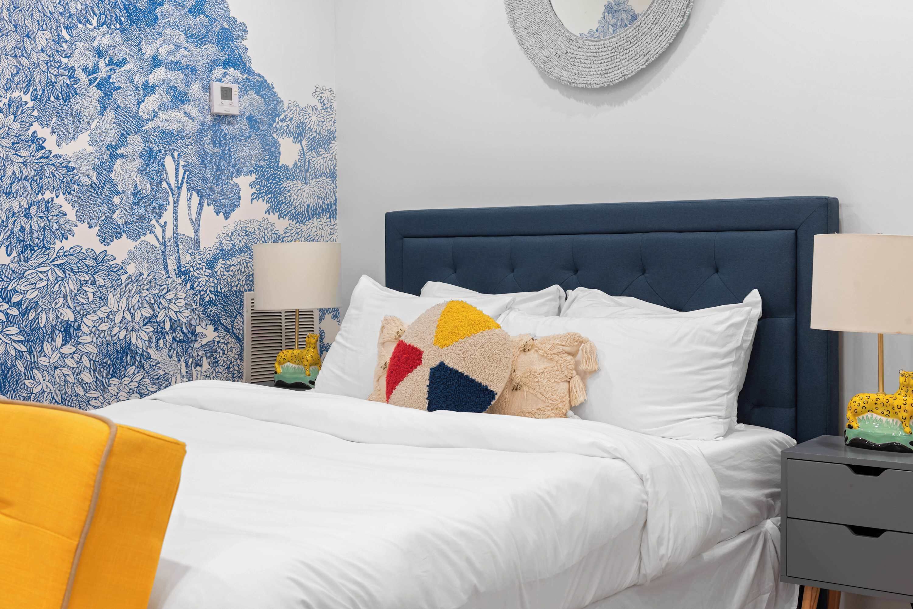 Una cama bien hecha con cabecera azul, ropa de cama blanca y almohadas coloridas.