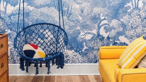 A room with a blue hanging chair, a yellow sofa, and a patterned wallpaper. - The Fox Den (Atlanta)