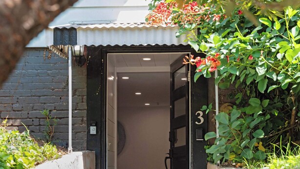 A narrow entrance to a building with a number '3' on the door, surrounded by greenery and a brick wall. - The Fox Den (Atlanta)