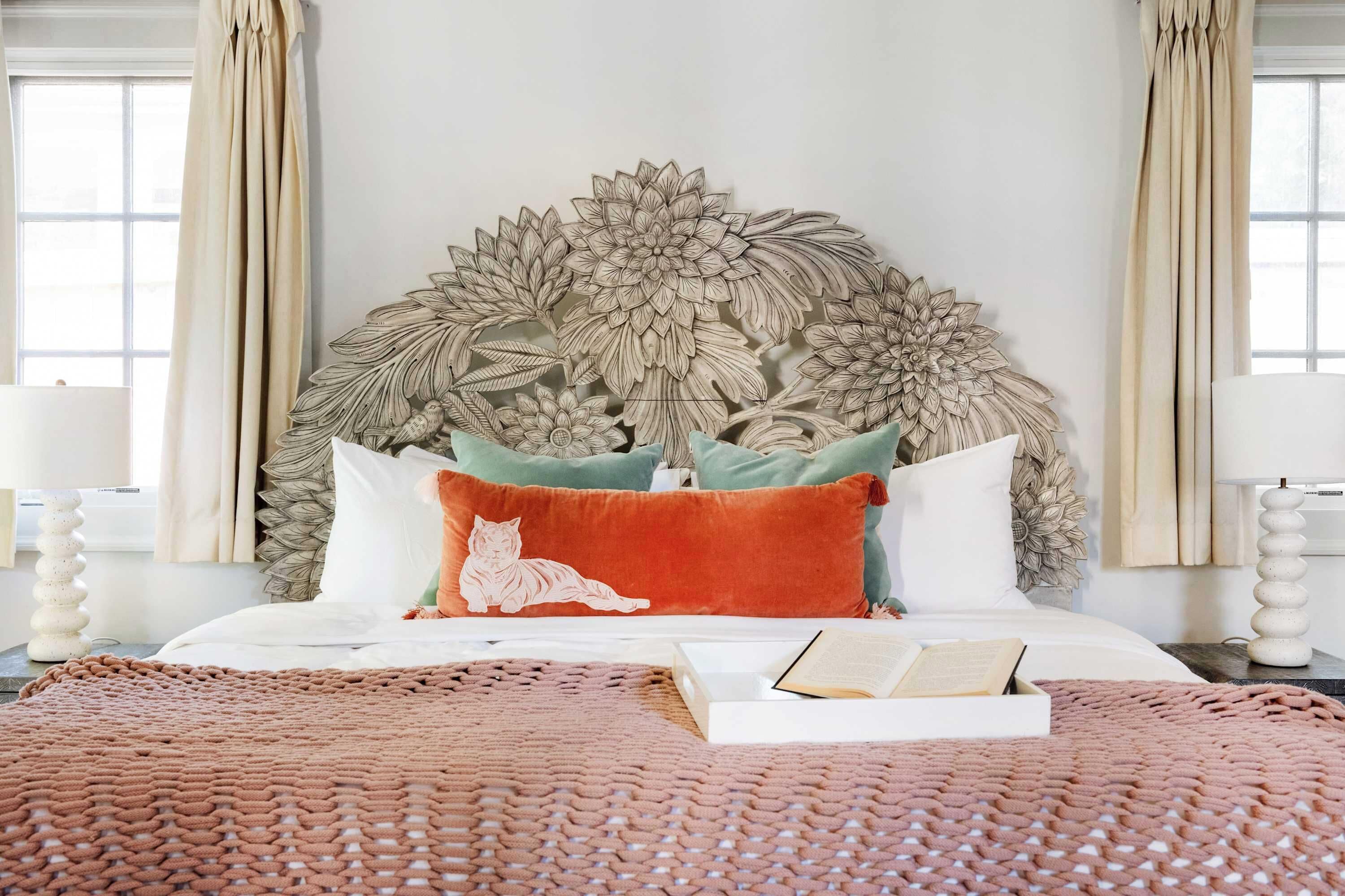 A neatly made bed with a large floral headboard, a red pillow with a cat design, and a book on the bed.