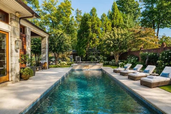 A rectangular swimming pool with lounge chairs and a stone building.