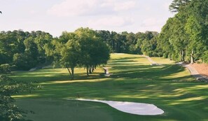 Ein Golfplatz mit einem Sandbunker, Bäumen und blauem Himmel.