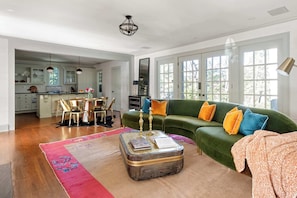 A spacious living room with a green sofa, a coffee table, and a dining area in the background.