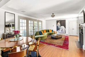 A spacious living room with a green sofa, a dining table with chairs, and a large painting on the wall.