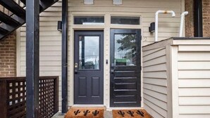 A front door with a dark-colored door and a window above it. There are two doormats with cactus designs in front of the door.