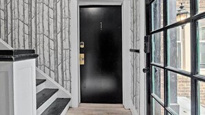 A black door with a number 1 sign, a white wall with a tree pattern, and a glass door on the right.