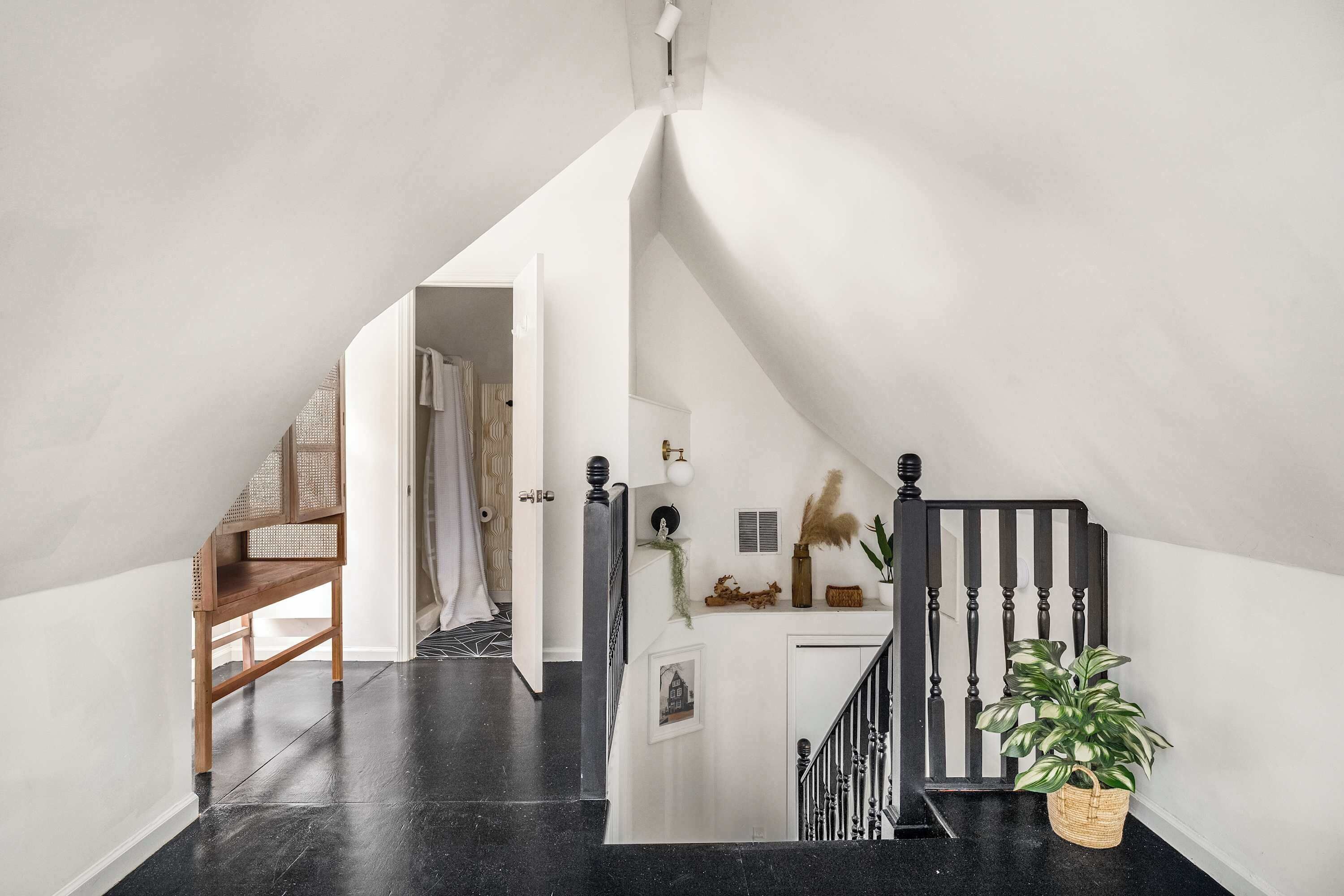 Um interior moderno com piso de mármore preto, um banco de madeira, escada com corrimão preto e uma planta em vaso.
