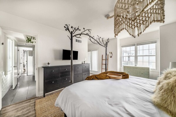 Un dormitorio con cama, cómoda, televisor y una planta decorativa.