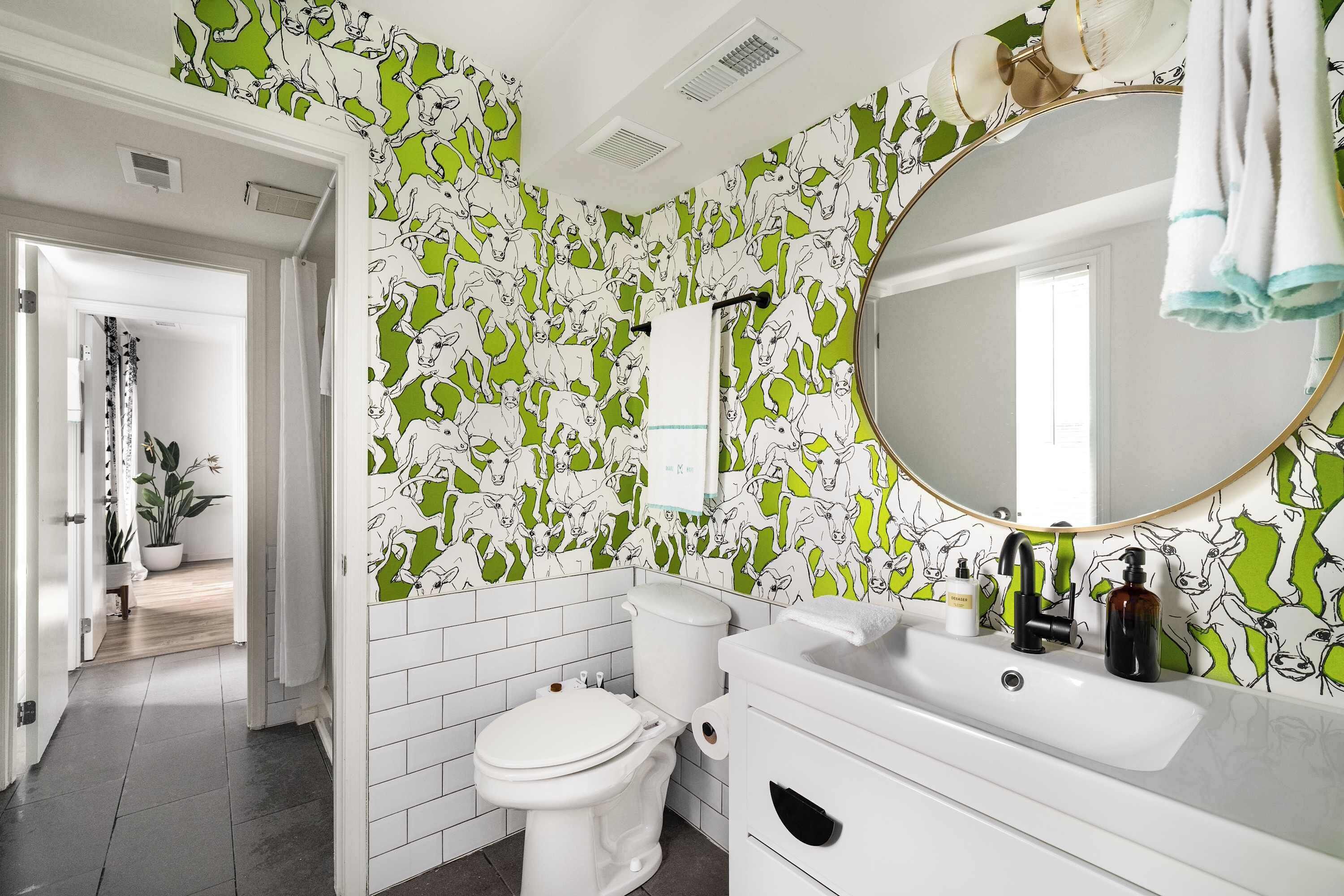 A bathroom with a toilet, sink, and mirror. The walls have a green and white pattern.