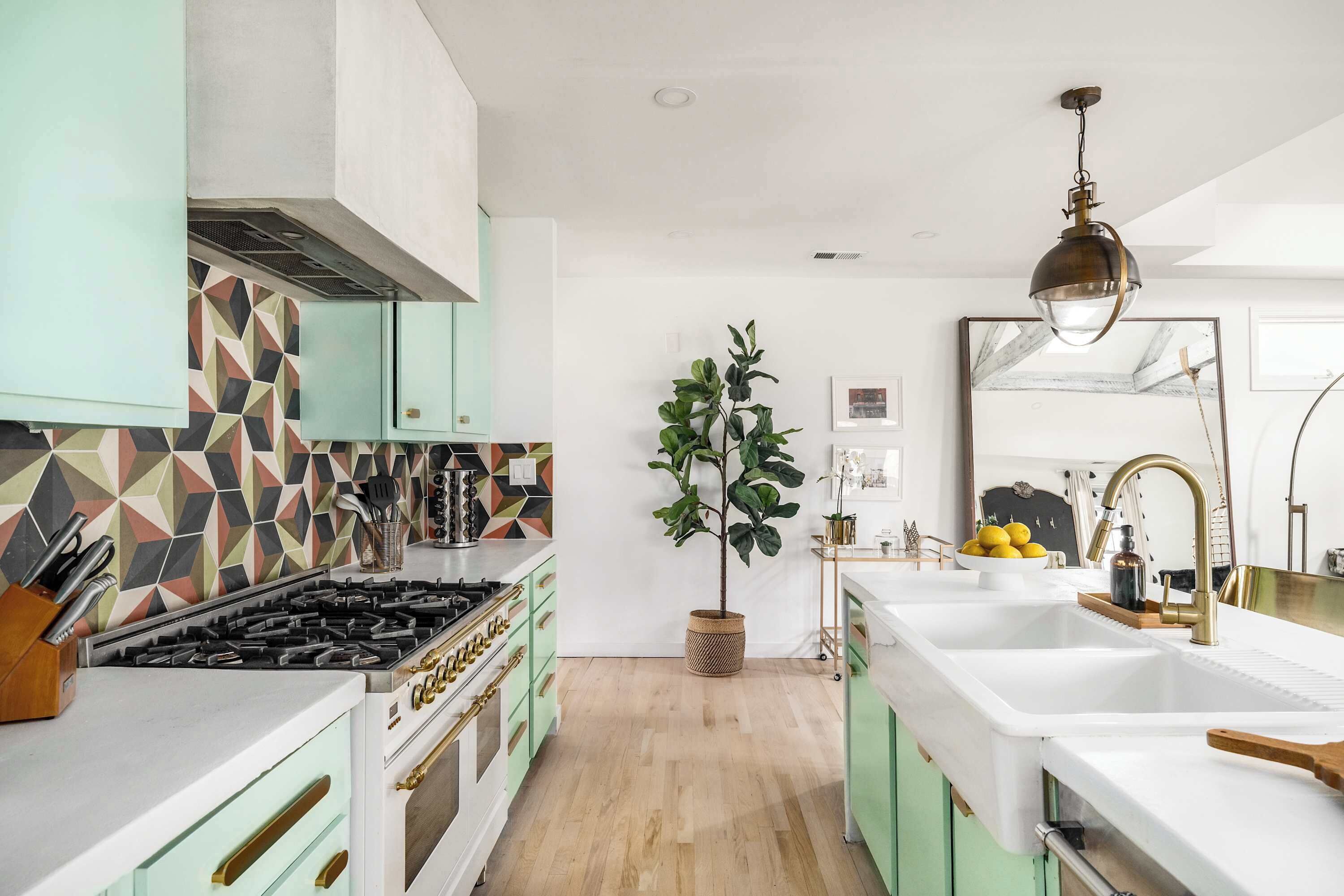 A kitchen with a gas stove, white cabinets, a large sink, and a hanging light fixture.