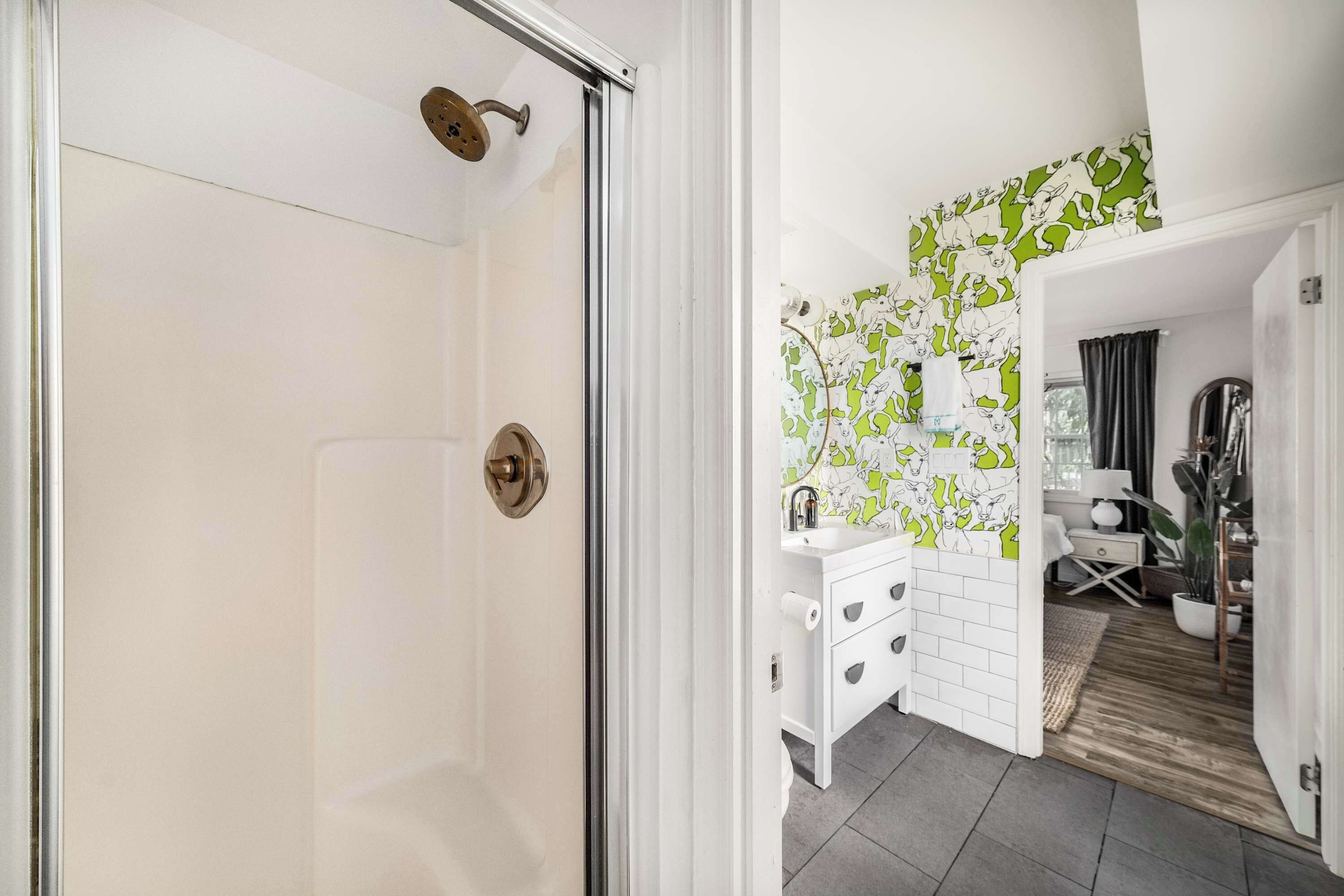 A modern bathroom with a glass shower door, white cabinetry, and a green and white patterned wall.