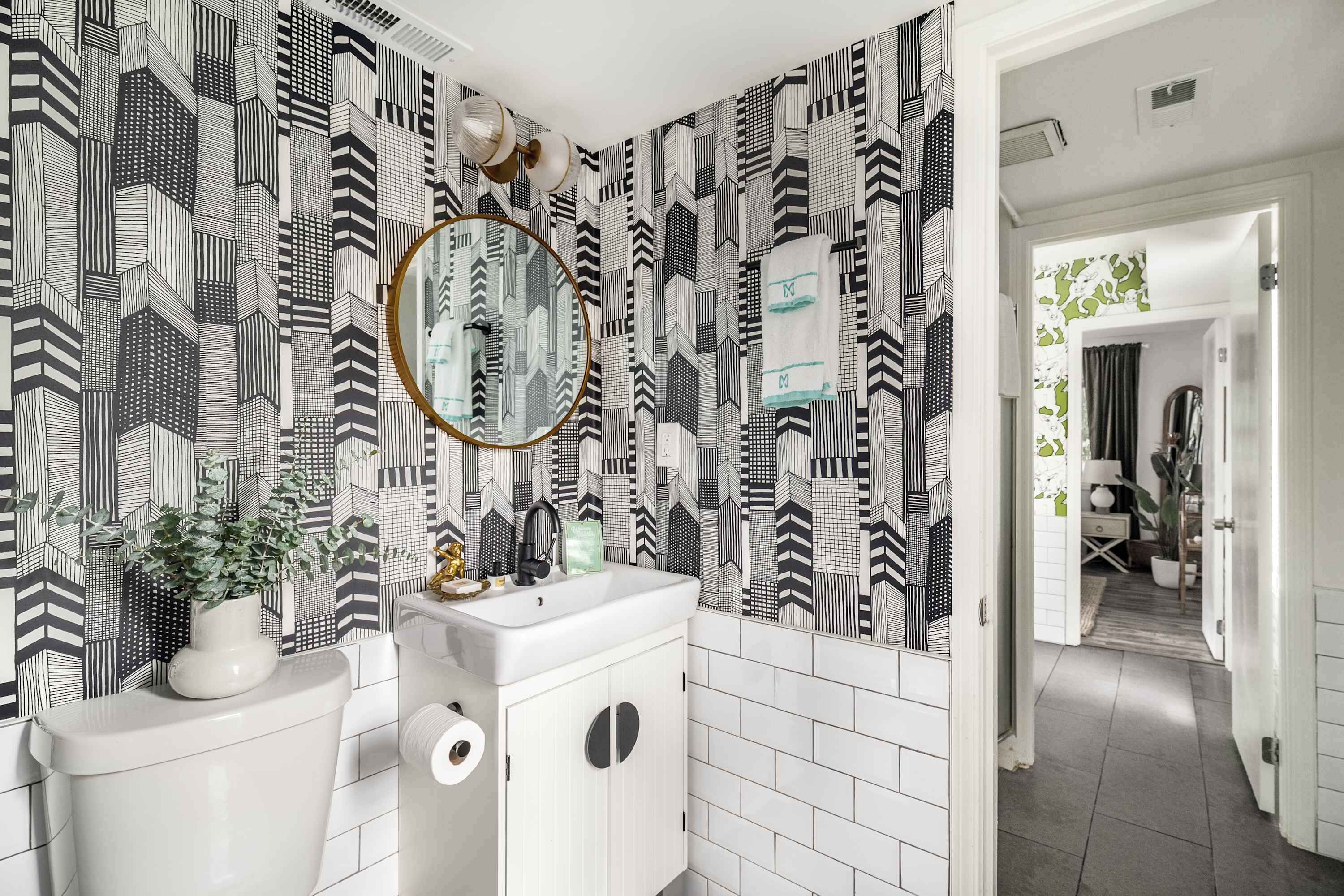 A bathroom with a black and white geometric patterned wall, a white sink, a mirror, and a toilet.