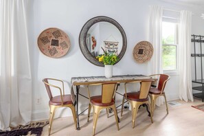 Uma sala de jantar com um piano, quatro cadeiras, um espelho redondo e obras de arte decorativas.