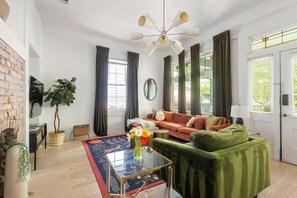 Uma sala de estar moderna com um sofá verde, um sofá vermelho, uma mesa de centro de vidro e uma parede de tijolos.