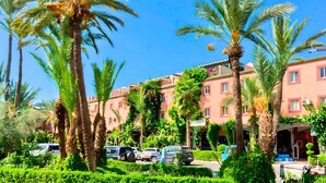 A hotel with multiple-story buildings, palm trees, and parked cars in the foreground. - Beautiful Riad in Marrakech with swimming pools (Marrakech)
