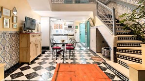 A spacious living area with a checkered floor, a dining table with chairs, a TV on a cabinet, and a staircase with decorative railings. - Beautiful Riad in Marrakech with swimming pools (Marrakech)