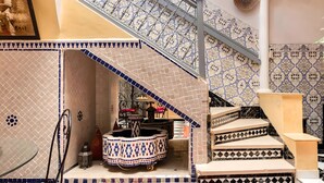 A staircase with patterned tiles, a round table with a patterned tablecloth, and a hanging basket. - Beautiful Riad in Marrakech with swimming pools (Marrakech)