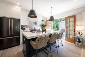 A modern kitchen with a large island, stainless steel appliances, and wicker bar stools.