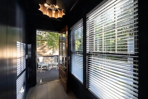 A corridor with a view of an outdoor seating area, a door, and a window with blinds.