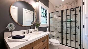 A bathroom with a vanity, a round mirror, a toilet, and a glass-enclosed shower.