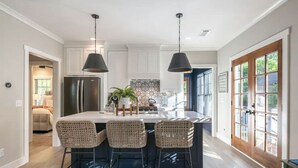 Een moderne keuken met een centraal eiland, twee hanglampen en uitzicht op de omgeving door een groot raam.
