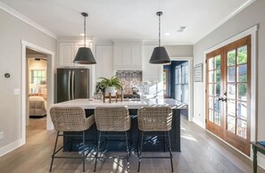 Una cocina moderna con una isla central, dos lámparas colgantes y vistas al exterior a través de un amplio ventanal.