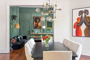 A dining area with a dark wooden table, white upholstered chairs, and a vase with red flowers. - Grand Damn (Atlanta)