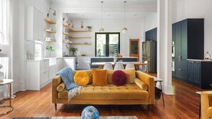 A modern living room with a mustard sofa, wooden shelves, and pendant lighting.