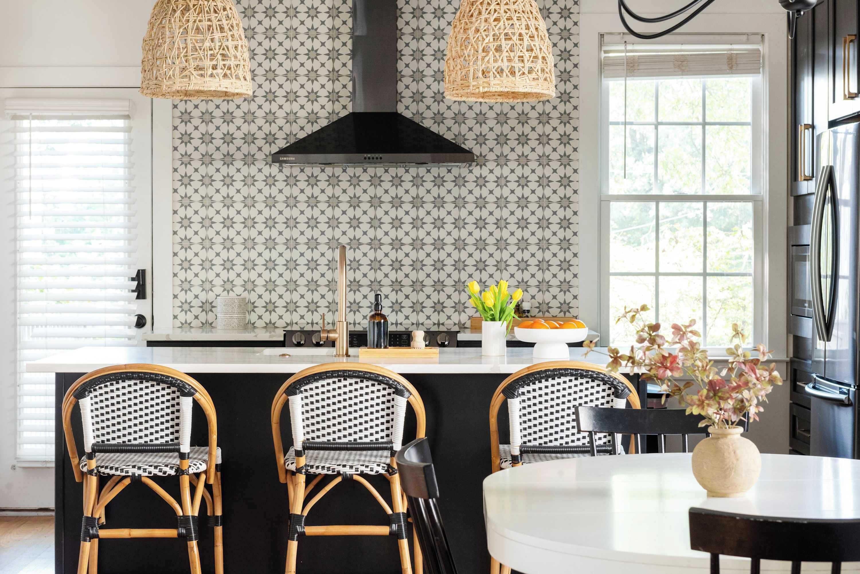 A kitchen with a black island, wicker chairs, and a large window.