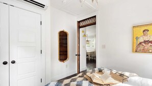 A bedroom with a bed, a bedside table with a book and a cup, a mirror, and a door. - The Sanctuary (Atlanta)