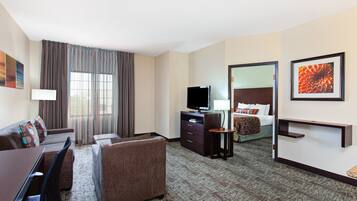 A hotel room with a sofa, a TV, a desk, a bed, and a mirror.