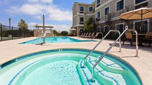 A swimming pool area with lounge chairs and umbrellas, surrounded by a building with multiple windows. - King Suite | Free Wi-Fi + Breakfast, Pool, Gym. (Lake Forest)