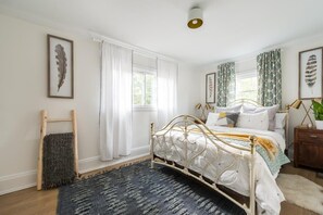 A bedroom with a bed, a wooden ladder, a rug, and curtains.
