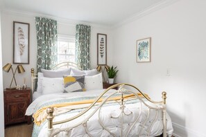 Un dormitorio con cama, cortinas, mesita de noche, lámpara y decoración en la pared.
