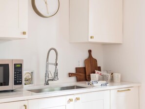 A modern kitchen with white cabinetry, a stainless steel sink, a microwave, and a wooden cutting board. - Buchanan (Atlanta)