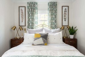 A bedroom with a bed, two nightstands, a window with curtains, and framed artwork on the walls. - Buchanan (Atlanta)