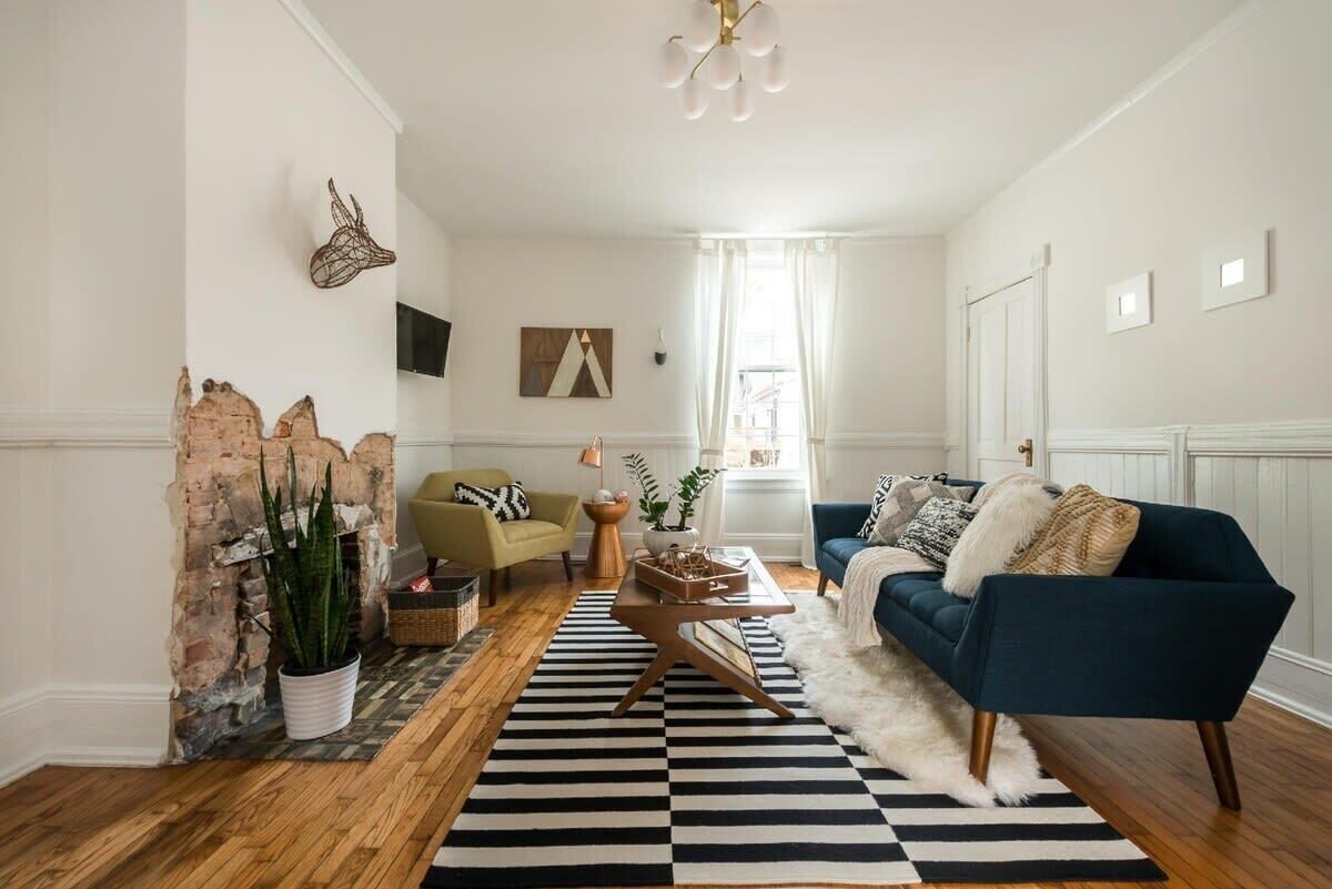 A living room with a blue sofa, a wooden coffee table, a striped rug, and a brick wall.