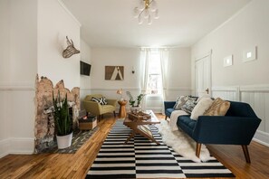A living room with a blue sofa, a wooden coffee table, a striped rug, and a brick wall.