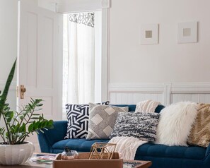 A living room with a blue sofa, patterned cushions, a white plant, and a wooden coffee table.